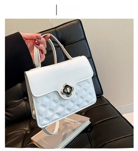 Detail of white quilted crossbody bag featuring elegant floral lock and leather handle