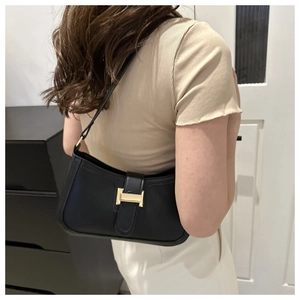 Close-up of black crossbody bag featuring a distinctive gold H-shaped metal buckle detail