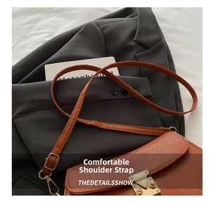 Close-up of brown lychee-grain leather shoulder bag with metallic buckle on a grey suit