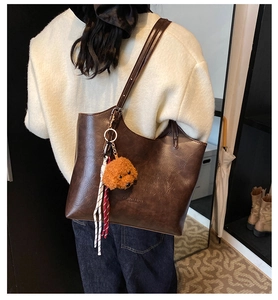Dettaglio della texture in pelle vintage e del ciondolo a cane su una borsa a secchiello