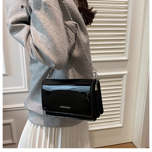 Detail of black patent leather flap bag with silver chain strap and Sunila Fashion text