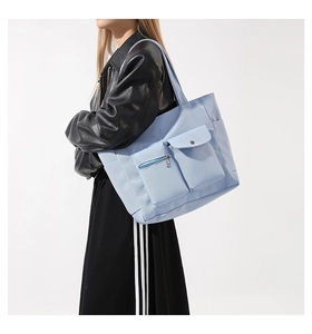 Detail of light blue nylon tote bag showing metal zipper and snap button pockets