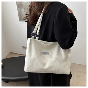 Detail of off-white corduroy tote bag showing ribbed texture and metal ring shoulder straps