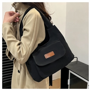 Close-up of black canvas tote bag featuring a leather patch detail and front flap pocket