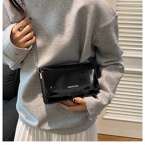 Detail of black patent leather crossbody bag with silver chain strap and branding