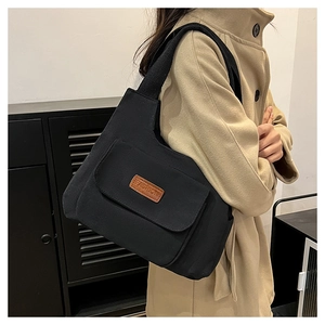 Detail of black canvas tote bag with fashion leather patch worn by model over a coat