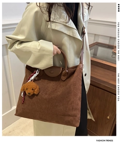 Détail d'un sac cabas en daim marron avec anses en cuir et breloque ours en peluche