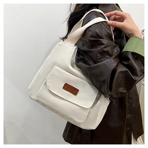 Detail of white canvas tote bag with front flap pocket and brown leather fashion tag