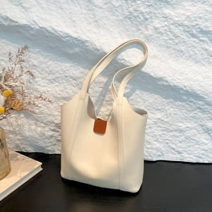 Minimalist beige tote bag with brown leather clasp against a rustic stone wall