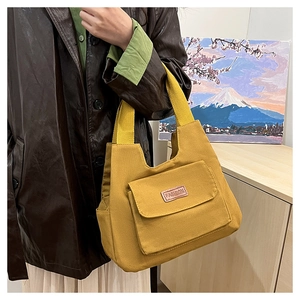 Detail of ginger yellow canvas tote bag featuring front flap pocket and fashion label