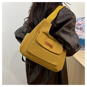Detail view of mustard yellow canvas bag with leather logo and functional front pockets