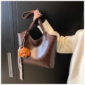 Dettaglio di borsa a secchiello in pelle cerata marrone con ciondolo a orso e logo