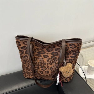 Sac cabas léopard avec anses en cuir marron et pendentif ours sur un canapé noir