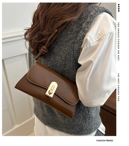 Detail view of a vintage brown leather baguette bag with a gold buckle worn by a model
