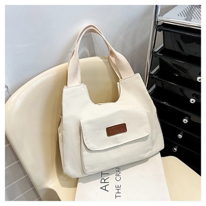 Detail of canvas tote bag featuring front pocket with brown leather fashion label