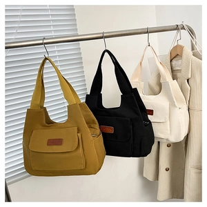 Three canvas tote bags in yellow, black, and beige with front pockets and wide straps