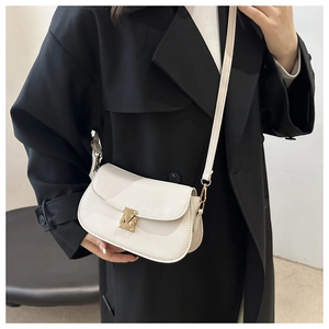 Detail of off-white lychee grain leather crossbody bag with gold metal clasp on black coat