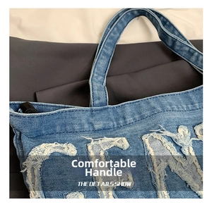 Close-up of denim tote bag showing frayed letter details and durable handle stitching