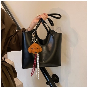 Dettaglio borsa tote in pelle PU nera con ciondolo a forma di cane in peluche marrone