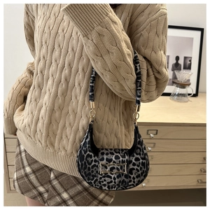 Detail of trendy leopard print hobo bag with gold hardware worn by a model in a cozy setting