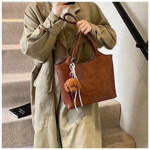Dettaglio di una borsa tote marrone in pelle con ciondolo a cane di peluche e logo stampato