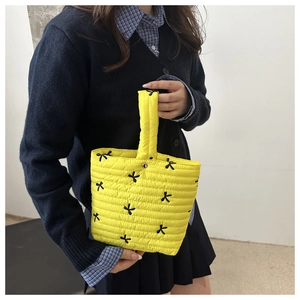 Detail van gele gewatteerde handtas met zwarte geborduurde strikjes en compact design