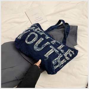Detail of blue denim tote bag with YOUTHER fringed letter applique and shoulder straps