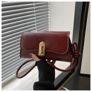 Detail of dark red vintage crossbody bag featuring a golden lock and textured leather