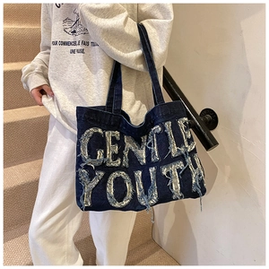 Detail of blue denim tote bag with frayed GENTLE YOUTH lettering and street style design