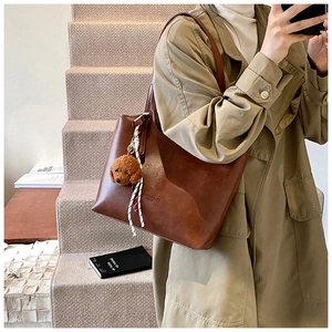 Close-up of brown PU tote bag with bear charm and embossed fashion letters