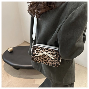 Detail of leopard print crossbody bag with white bow and thick strap worn by model