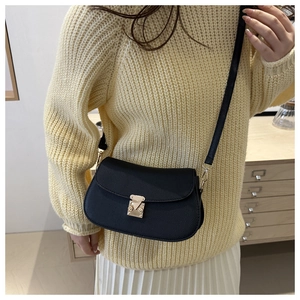 Detail of black pebbled leather crossbody bag with gold metal lock on woman's shoulder