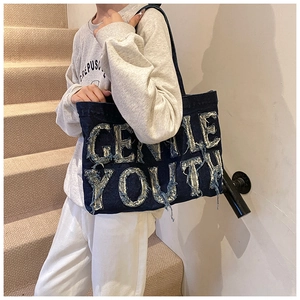 Close-up of vintage denim tote bag featuring frayed GENTLE YOUTH letter patch details
