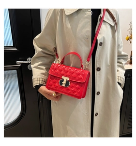 Detail of red quilted crossbody bag featuring a gold-tone T-shaped metal lock and leather strap