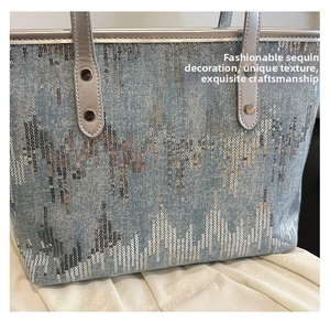 Close-up of light blue denim tote with silver sequins and metallic handle detail