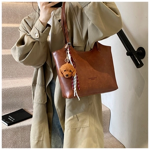 Detail of brown leather tote bag with plush puppy pendant and checkered ribbon decoration
