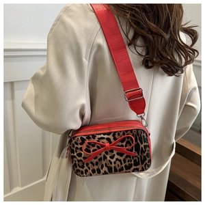 Fashionable leopard print crossbody bag with red ribbon bow worn over a beige coat