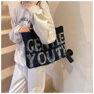 Detail of GENTLE YOUTH denim tote bag showing distressed fabric texture and large letters