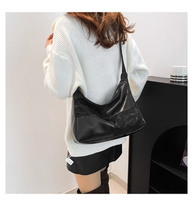 Detail shot of the glossy black hobo bag with contrast stitching on a model's shoulder