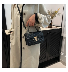 Detail of classic black quilted small square bag with golden T-lock and leather handle