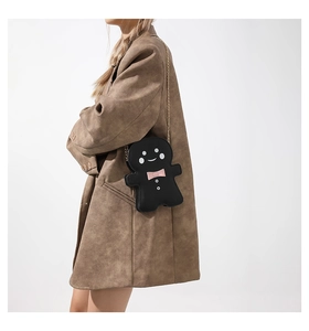 Creative black gingerbread man bag with pink bow and golden chain strap on a brown coat