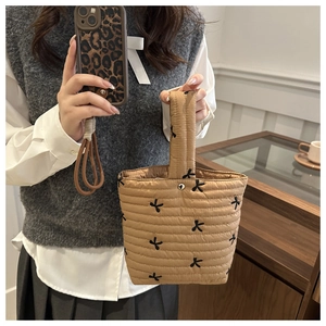 Dettaglio borsa a secchiello trapuntata beige con fiocchi neri e manici imbottiti