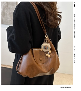 Detail of a brown vintage tote bag with flap closure and a plush charm on a black coat