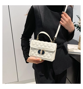Detail of quilted white crossbody bag featuring a golden metal twist lock and top handle