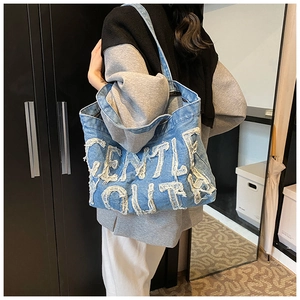 Detail of blue denim tote bag with white frayed Gentle Youth applique and shoulder strap