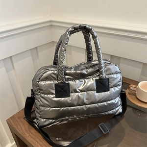 Silver quilted puffer tote bag with black strap on wooden table in a cozy setting