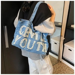 Close-up of blue denim tote bag with frayed 'GENTLE YOUTH' patch and long shoulder strap