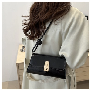 Detail of black glossy leather shoulder bag with a gold oval clasp and knotted strap
