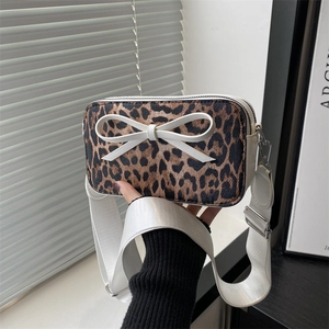 Niche leopard print camera bag with a white bow and wide strap shown in hand