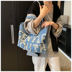 Detail view of denim tote bag featuring distressed Gentle Youth lettering and raw edges